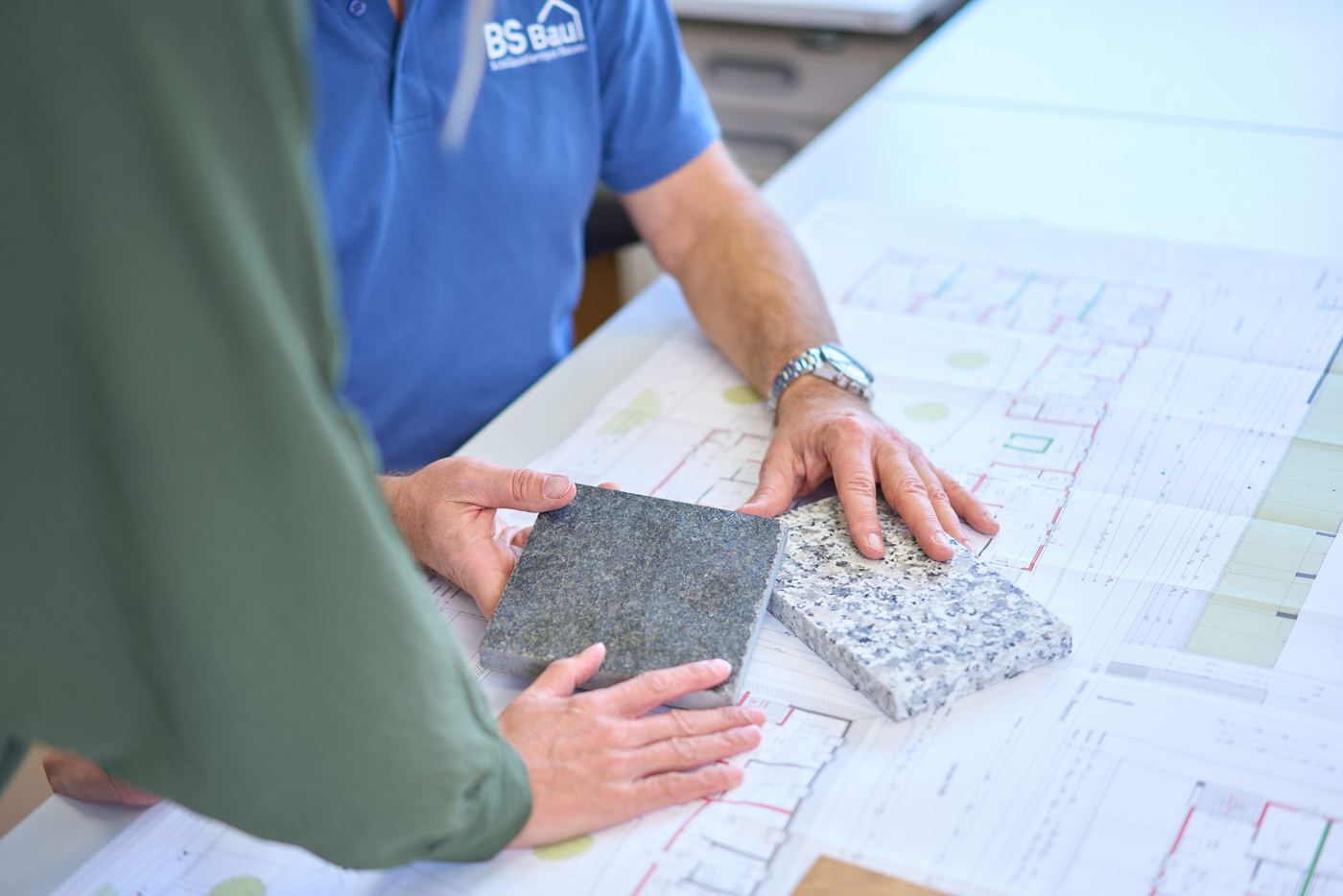 Zwei Mitarbeiter besprechen Materialmuster über einem Bauplan